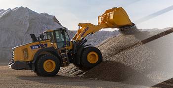 A Komatsu wheel loader in a quarry, dumping a load of gravel with a mountain in the background.
