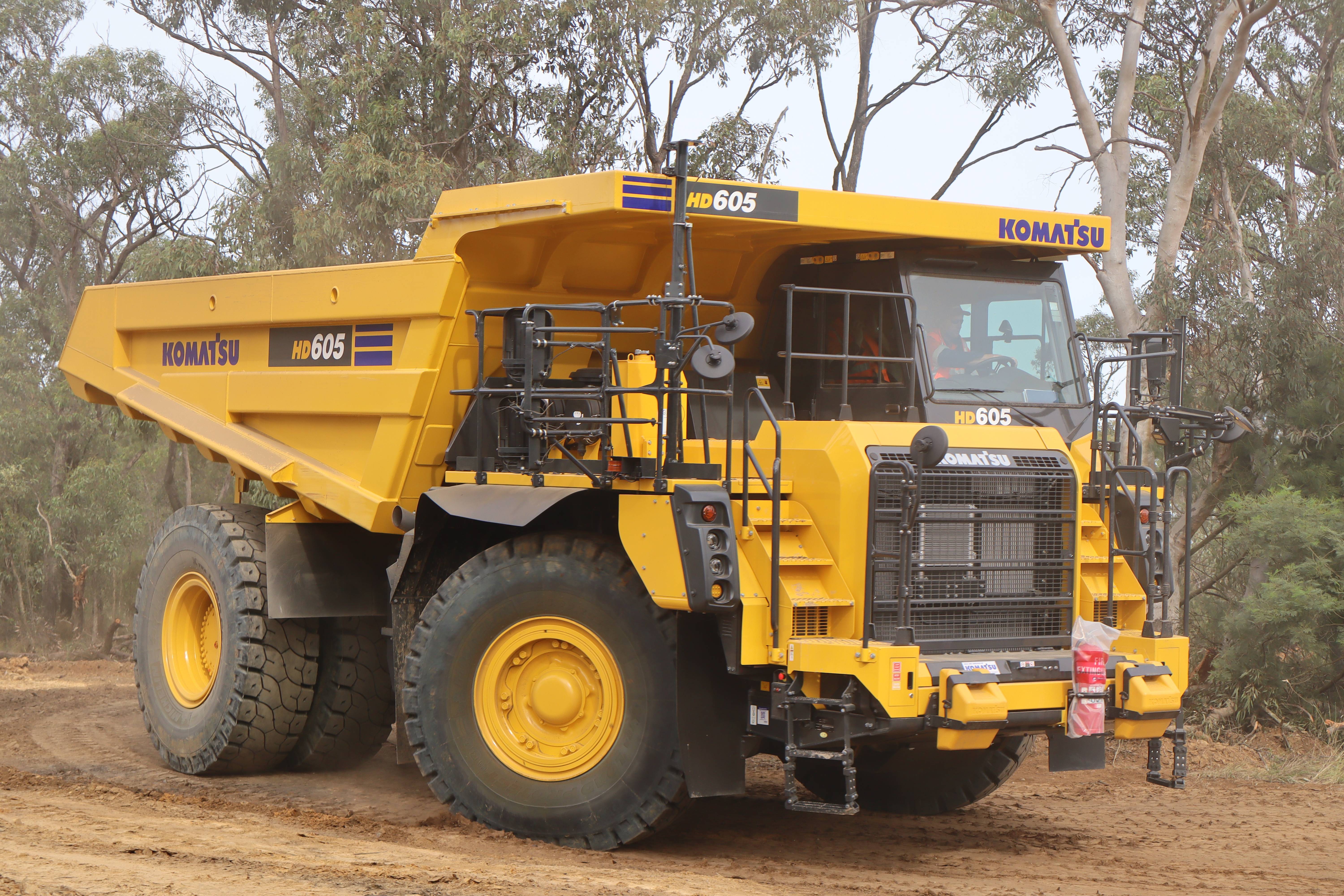 A Komatsu HD605 dump truck on a dusty road surrounded by light fog.