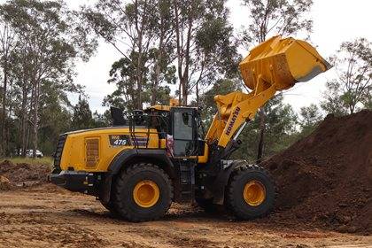 Komatsu WA475 wheel loader dumping soil in a wooded area.