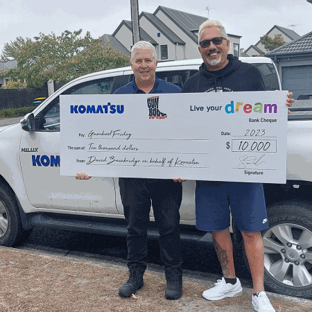 Two men standing in front of vehicle holding large cheque prop
