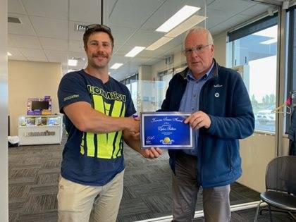 Two individuals presenting an award certificate inside an office.