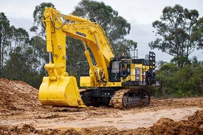 A large yellow Komatsu excavator on a worksite with orange-coloured dirt.