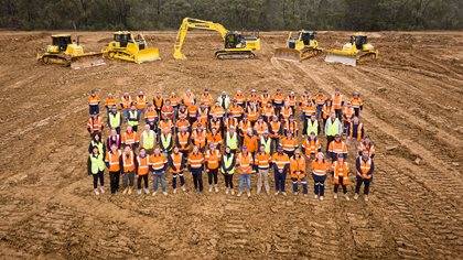Group of people in high-visibility vests standing together in front of heavy machinery on a construction site.
