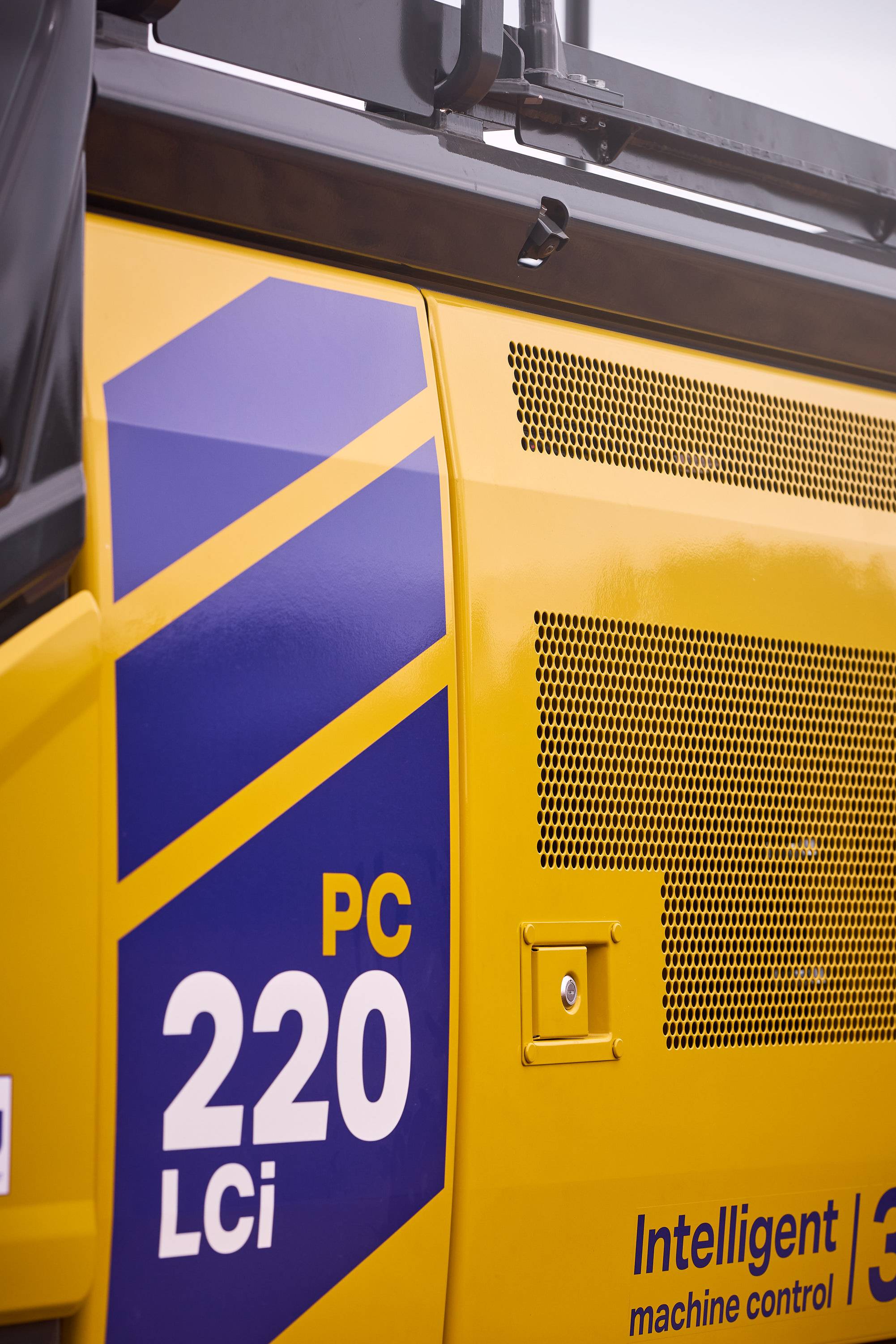 Close-up of a Komatsu PC220LCi excavator showcasing its yellow and blue livery and "Intelligent Machine Control" label.