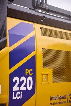 Close-up of a Komatsu PC220LCi excavator showcasing its yellow and blue livery and "Intelligent Machine Control" label.