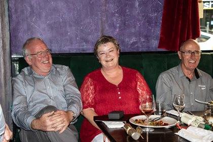 Three people enjoying a meal at a restaurant, sitting in front of a purple backdrop.