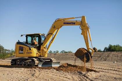 Komatsu excavator being operated to dig soil at a construction site with clear blue sky.