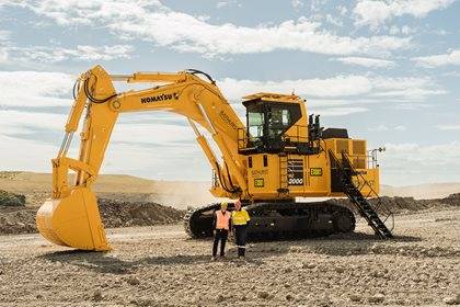 Two people in high visibility clothing standing in front of a large mining excavator on a mine site.