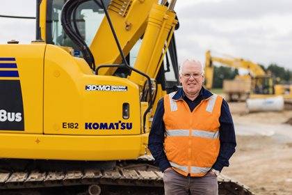 A person in a high-visibility vest stands in front of a Komatsu excavator on a construction site.